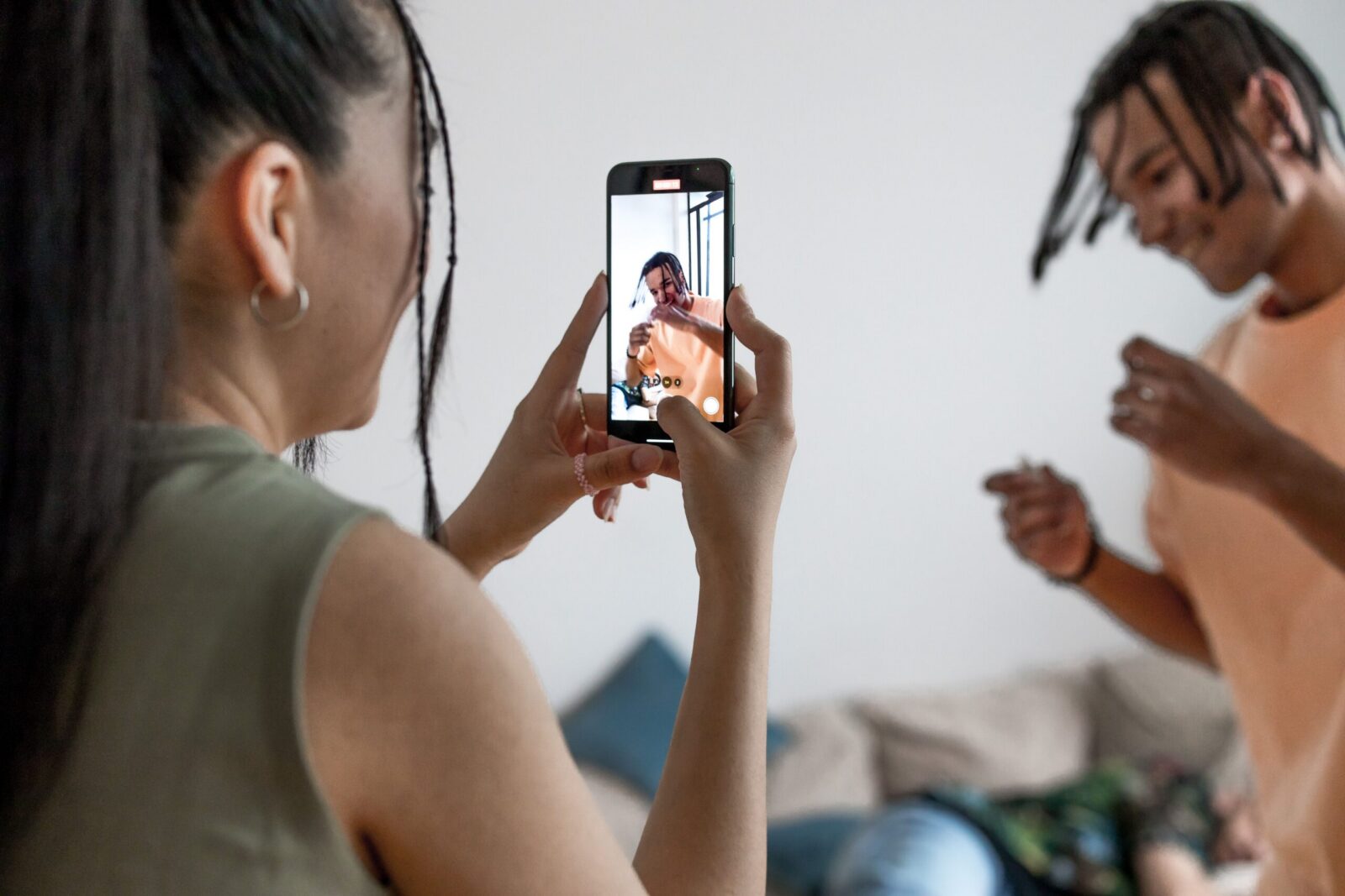 Two friends enjoying a fun, indoor vlogging session, capturing candid moments on a smartphone.
